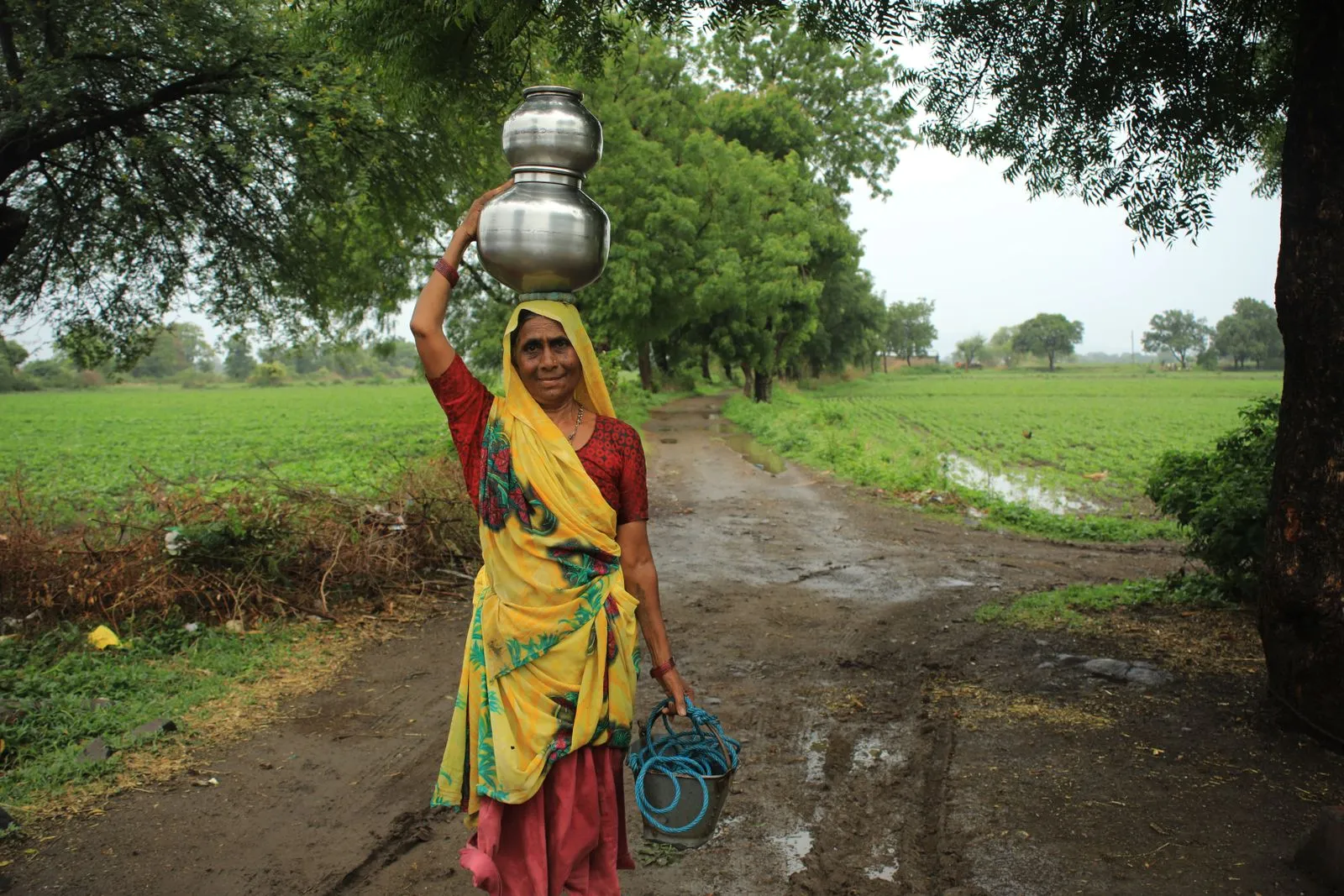 A woman carrying water pots along a village path