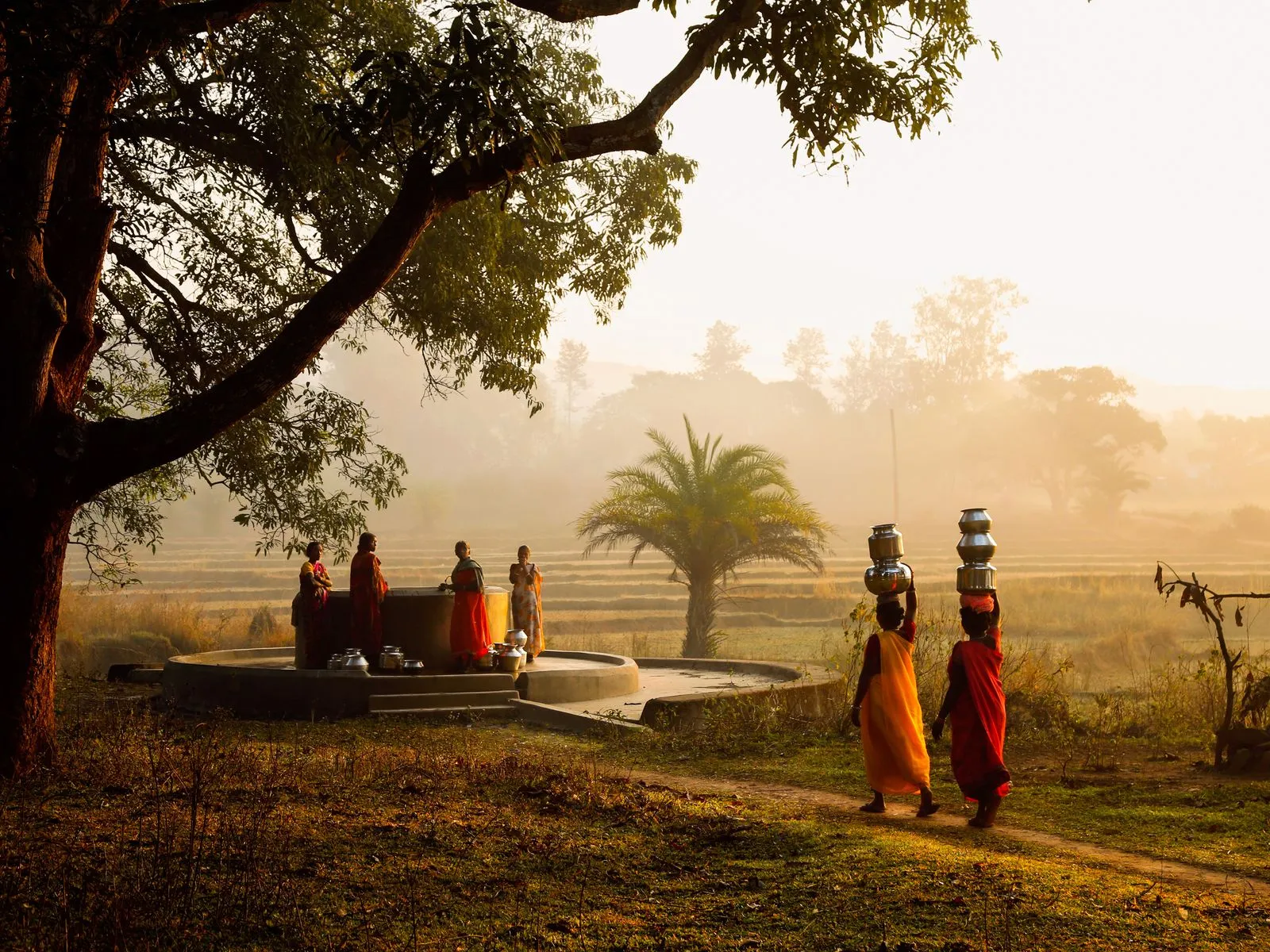Women carrying water pots beside a well at sunrise