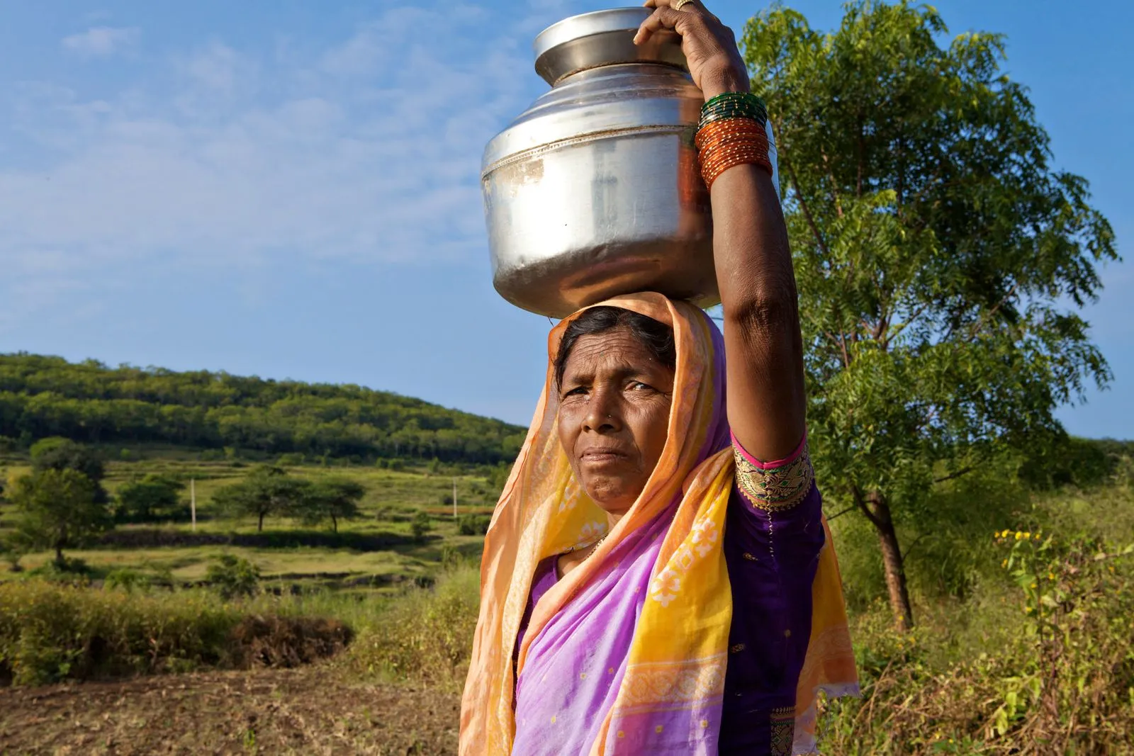 A woman carrying a metal water pot on her head