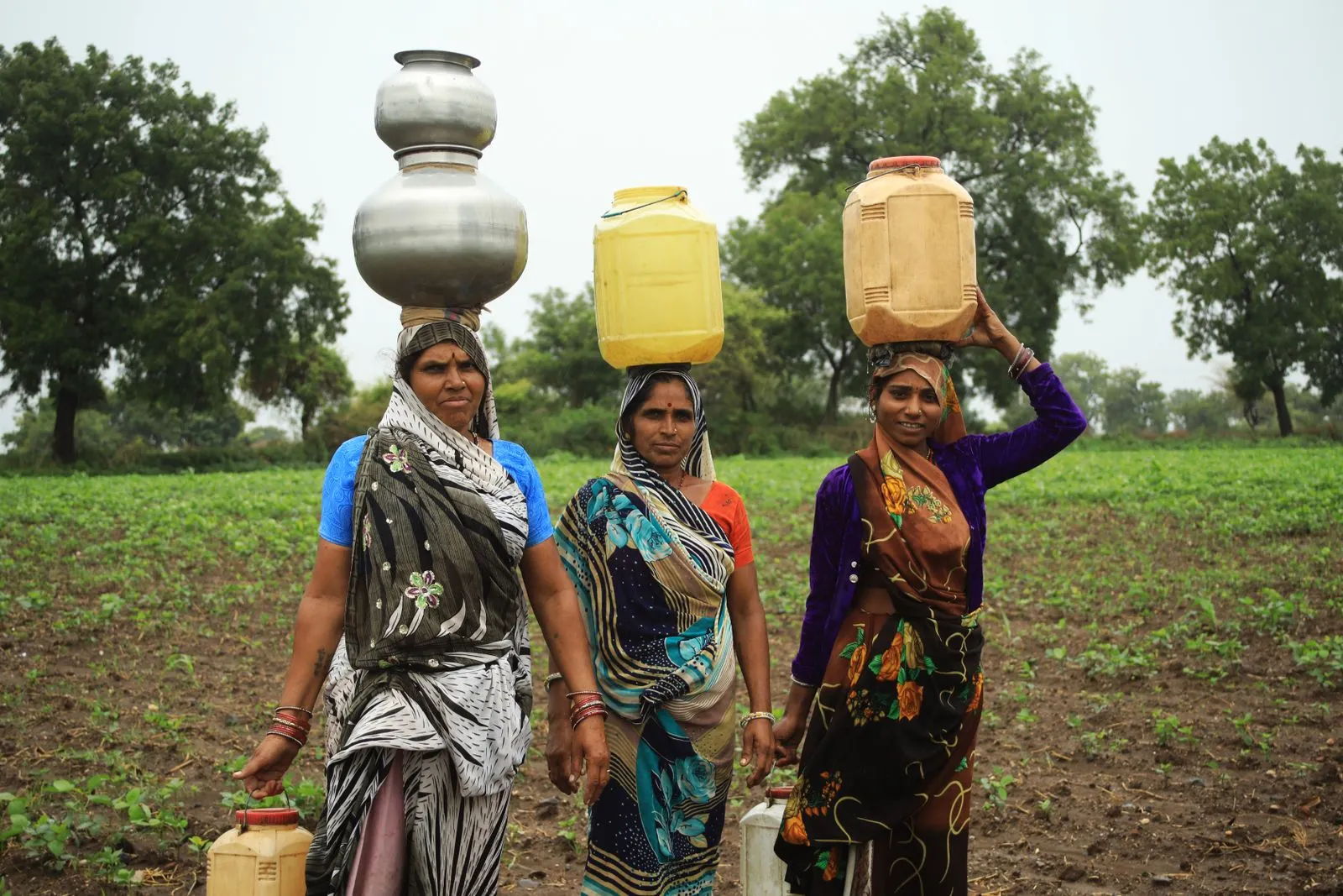 Three women carrying water across a field